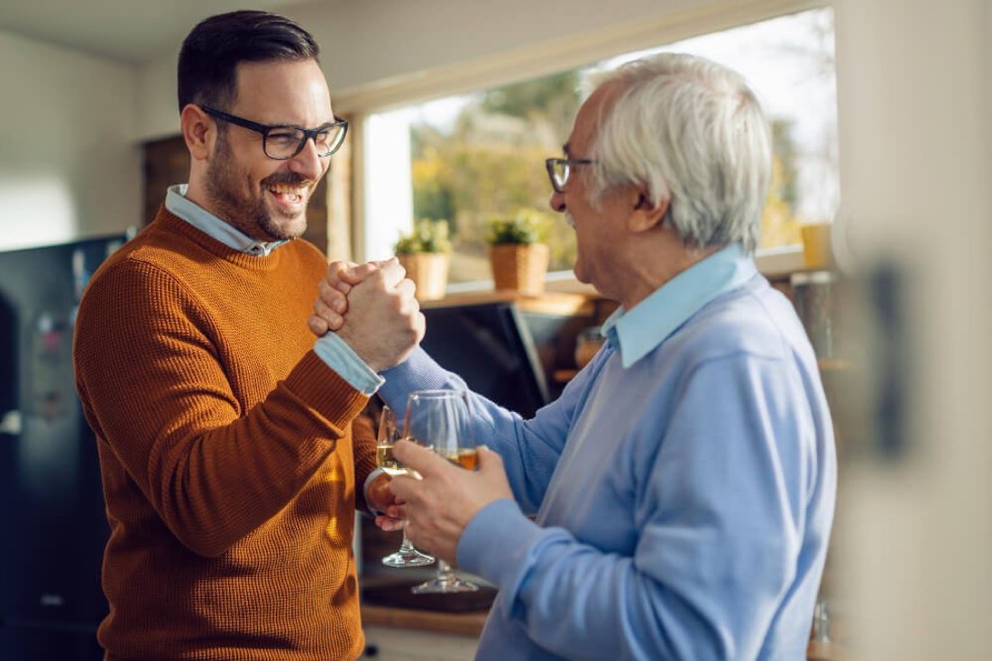 An adult son laughing with his elderly father at home